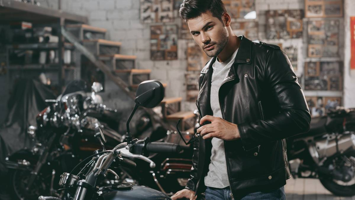Man wearing a black leather jacket beside a motorcycle